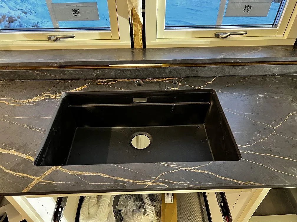 Underlimmad svart diskho i en matt Dekton Laurent köksbänkskiva med guldådring och fönsterbänk vid fönster i Gränna.