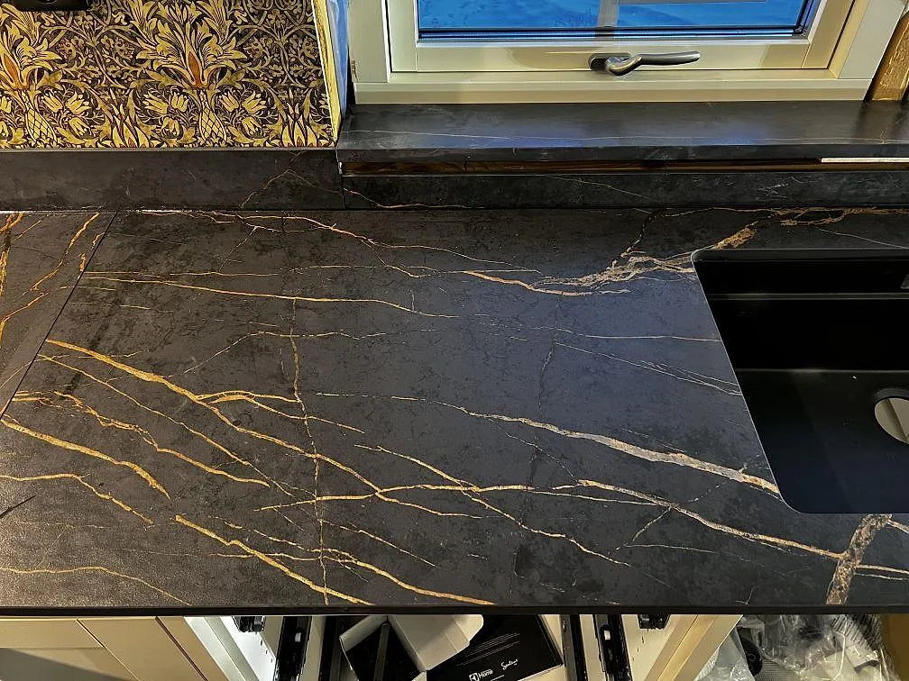 Detalj av matt Dekton Laurent köksbänkskiva med svart diskho, guldådring och fönsterbänk under montering i Gränna.
