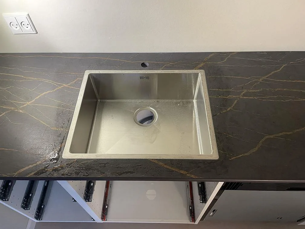 Underlimmad rostfri diskho infälld i matt mörk Dekton Laurent med guldådring, sedd uppifrån i ett kök i København S.