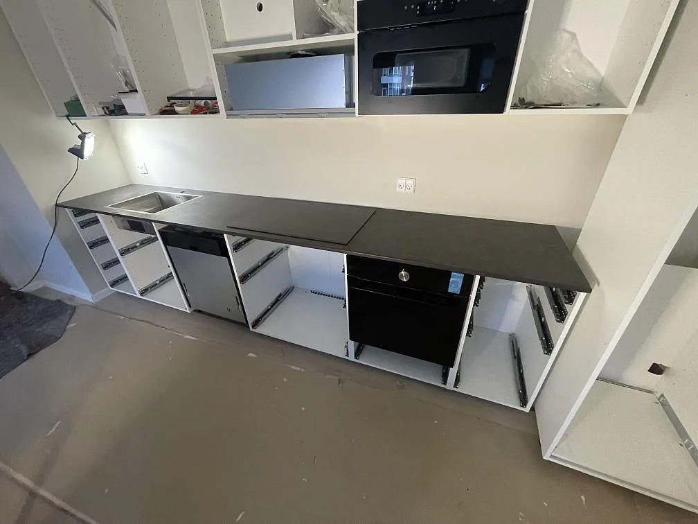 Köksbänkskiva i Dekton Laurent, matt mörk keramik med guldådring, lång rak bänkrad med rostfri diskho och induktionshäll i ett kök under montering i København S.