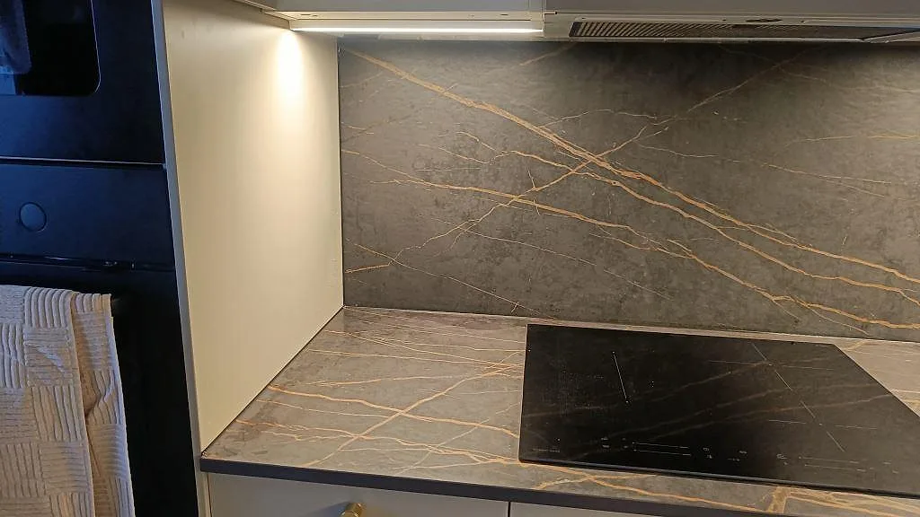 Dekton Laurent köksbänkskiva och stänkvägg i matt utförande med tydlig guldädring runt induktionshällen i ett kök i Malmö.