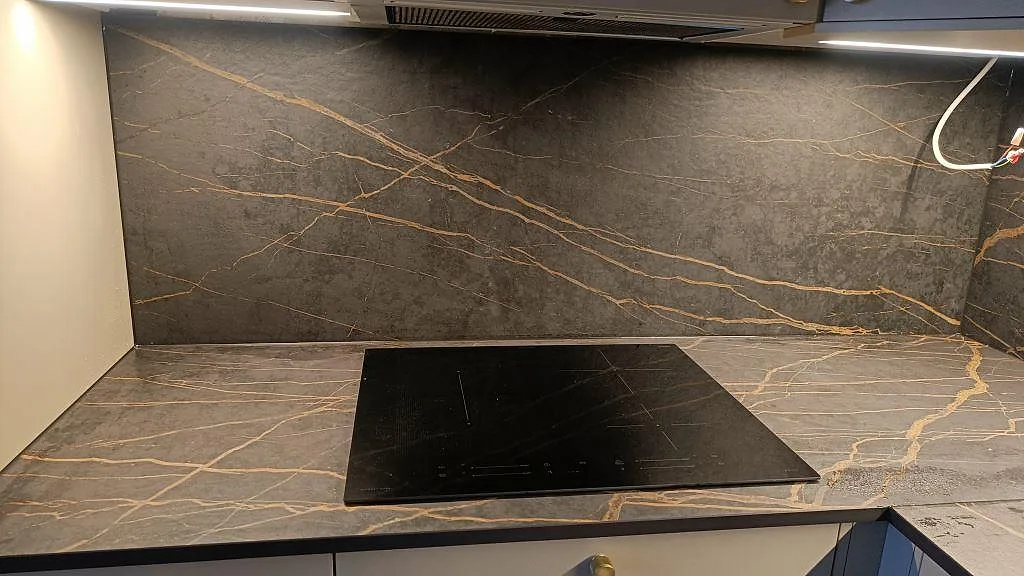 Matt Dekton Laurent stänkvägg och bänkskiva med kraftfull guld och kopparädring kring infälld induktionshäll i ett kök i Malmö.