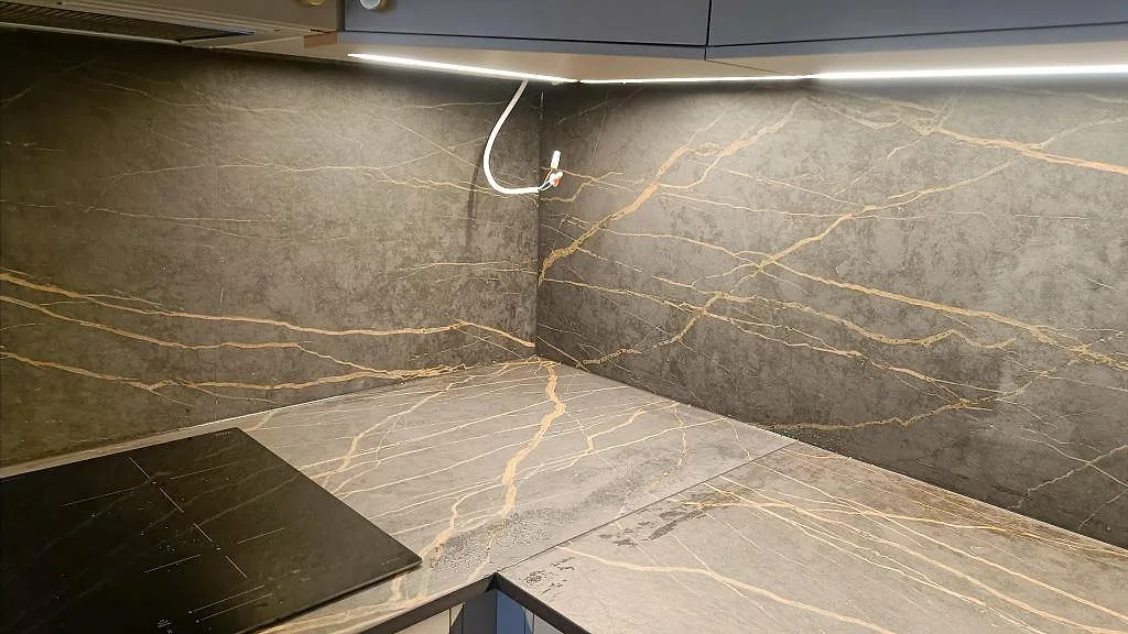 Hörnparti med Dekton Laurent bänkskiva och heltäckande stänkvägg i matt mörk keramik med guldädring i ett kök i Malmö.