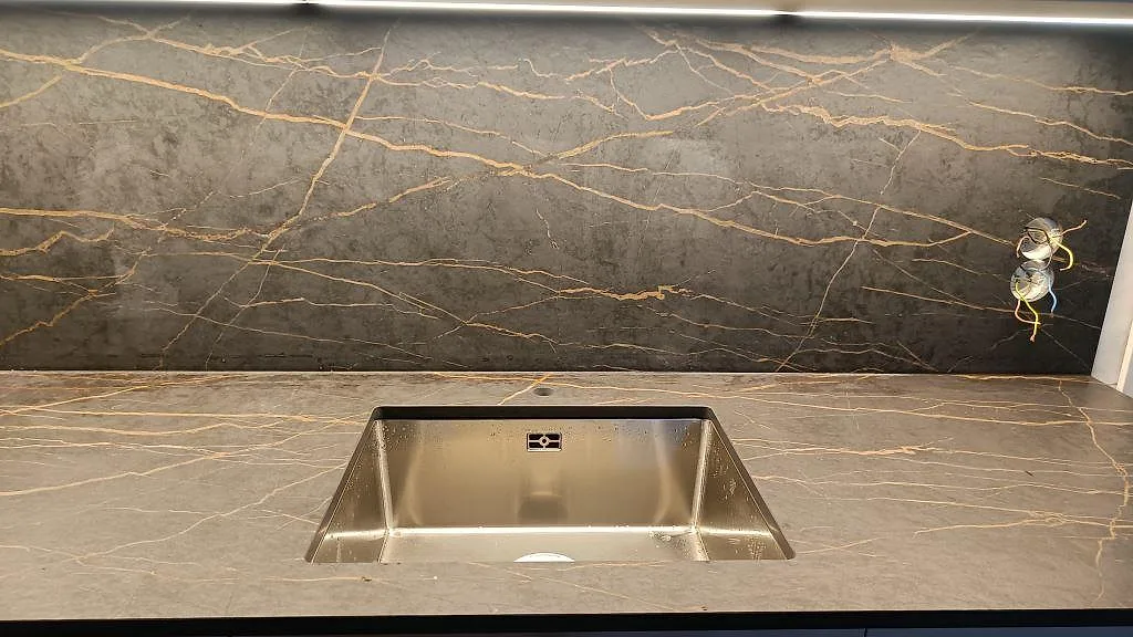Underlimmad rostfri diskho i matt Dekton Laurent bänkskiva med heltäckande stänkvägg och guldädring i ett kök i Malmö.