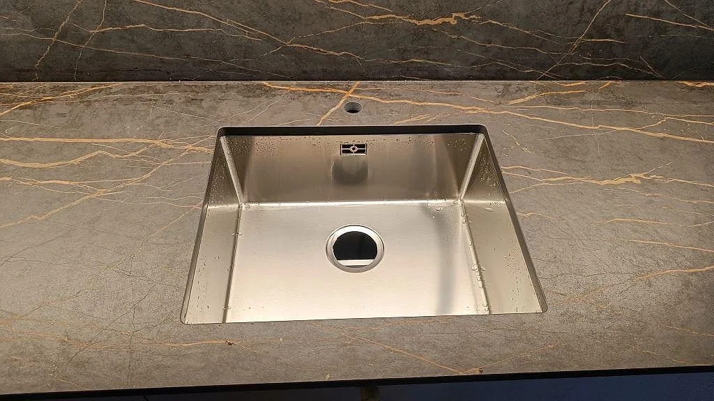 Detalj av underlimmad rostfri diskho i matt Dekton Laurent bänkskiva med guldädring i ett kök i Malmö.