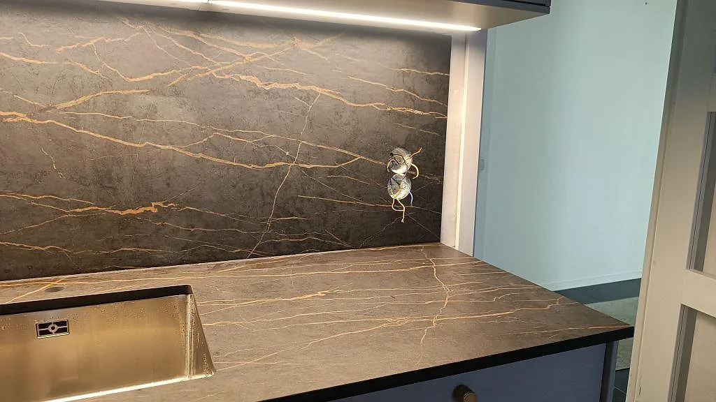 Dekton Laurent bänkskiva och heltäckande stänkvägg i matt mörk keramik med guldädring och underlimmad rostfri diskho i ett kök i Malmö.