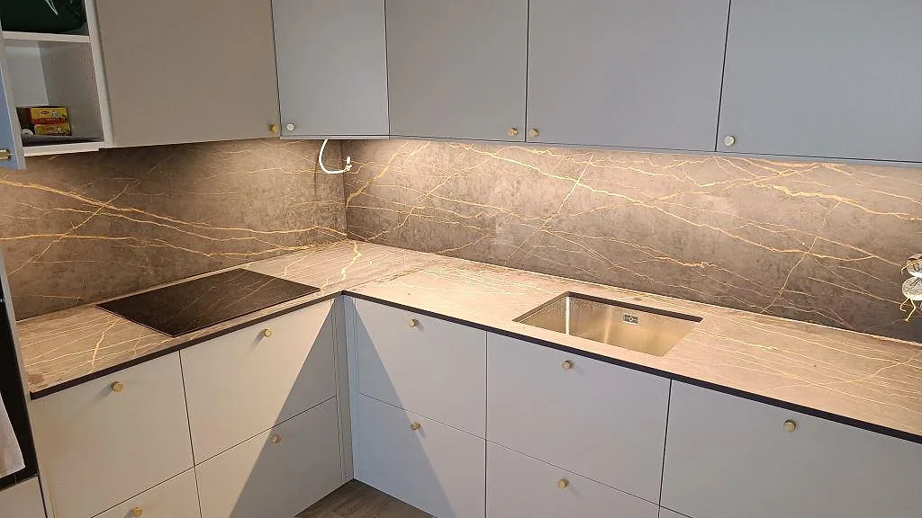 Köksbänkskiva i Dekton Laurent, matt mörk yta med guldädring, med heltäckande stänkvägg, underlimmad rostfri diskho och infälld induktionshäll i ett kök i Malmö.