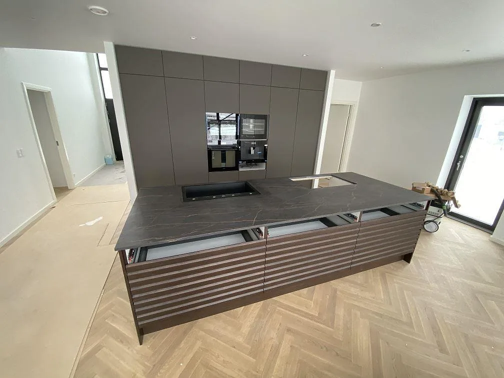Stor köksö i matt Dekton Laurent, keramik, med svart diskho ovanpå stenen och hälluttag i ett kök i Odense NØ.