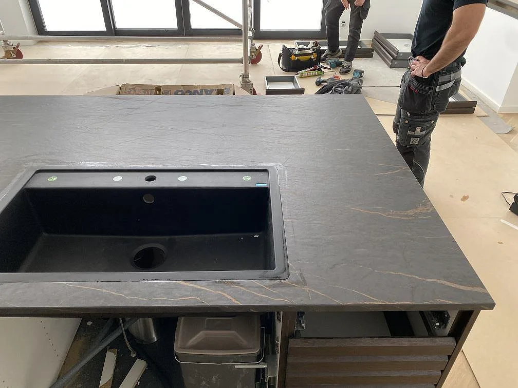 Matt köksbänkskiva i Dekton Laurent med svart diskho ovanpå stenen och mörk ådring under montering i Odense NØ.