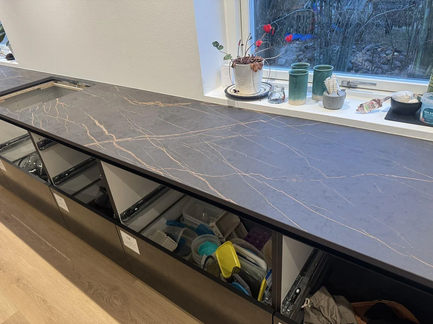 Lång köksbänkskiva vid fönster i matt Dekton Laurent, mörk keramik med varma ådror på öppna köksstommar i Odense SV.