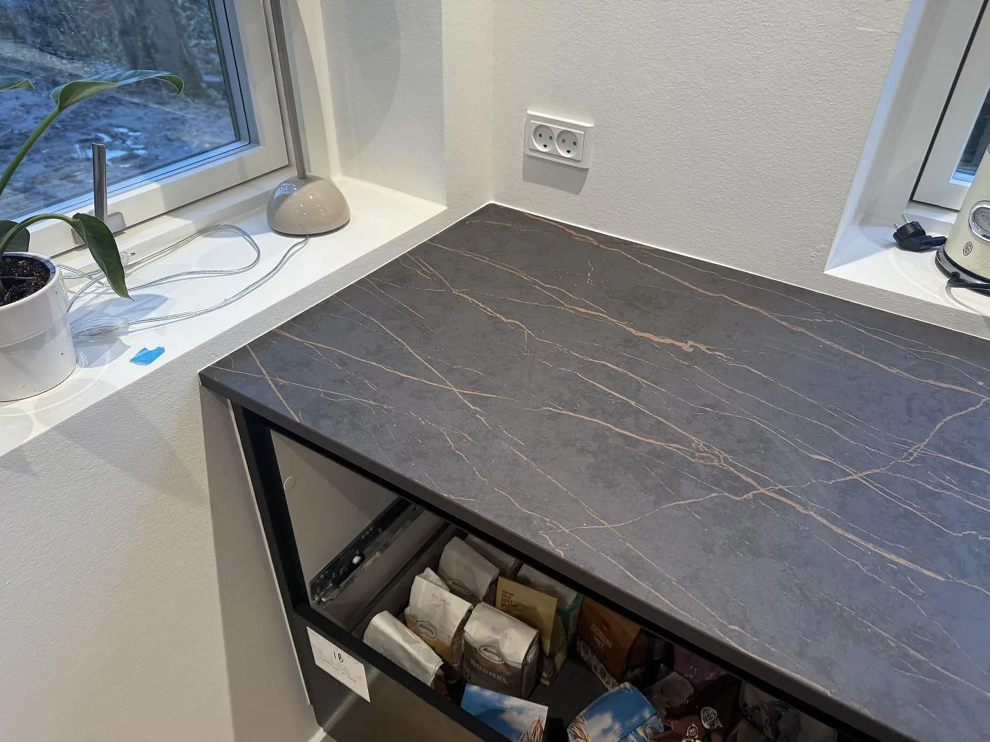 Hörnparti med köksbänkskiva i 20 mm matt Dekton Laurent vid fönster, monterad på öppna stommar i Odense SV.