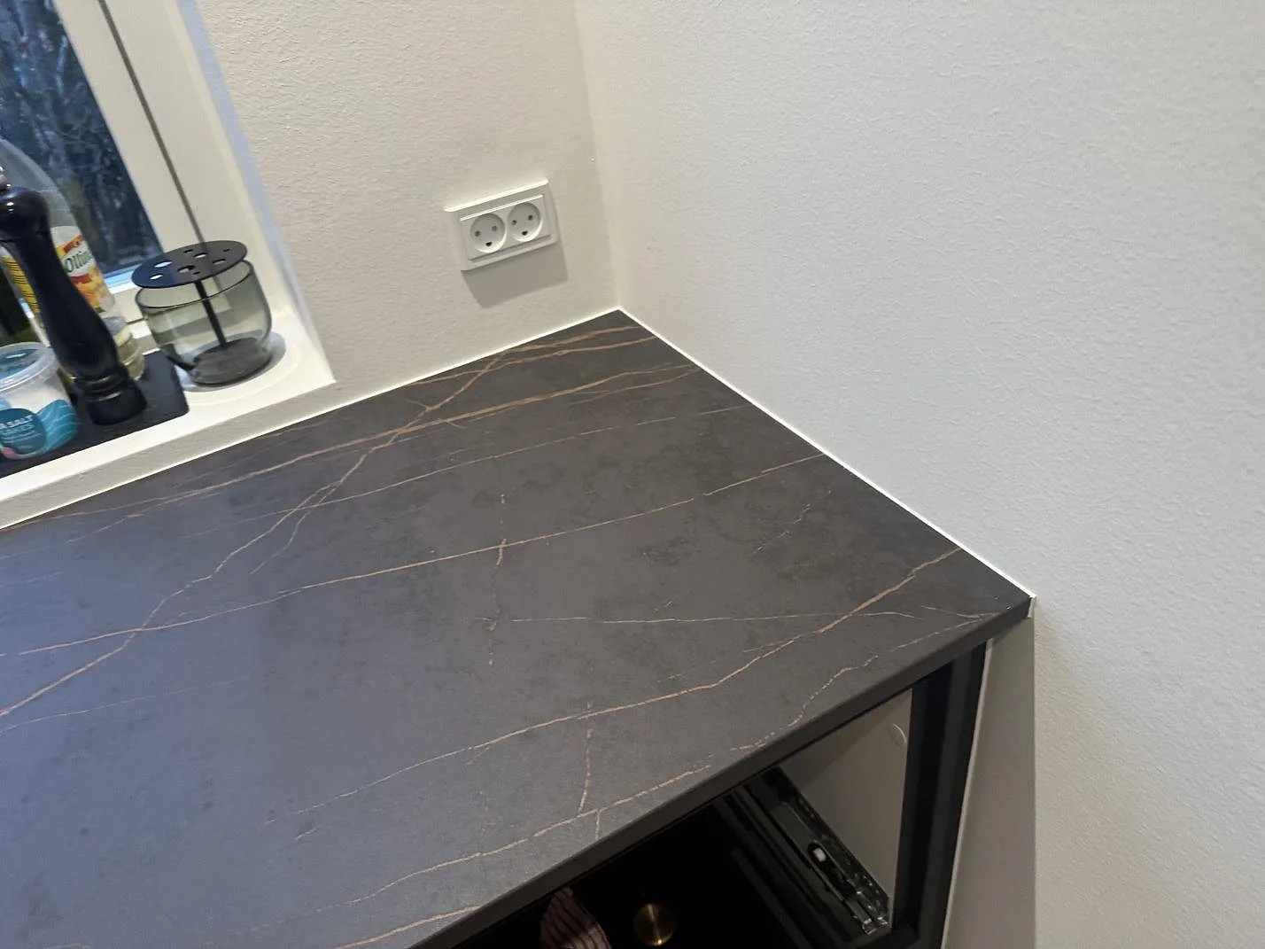 Detalj av bänkskiva i matt Dekton Laurent vid vägg och fönster, mörk keramik med diskret guldådring i Odense SV.