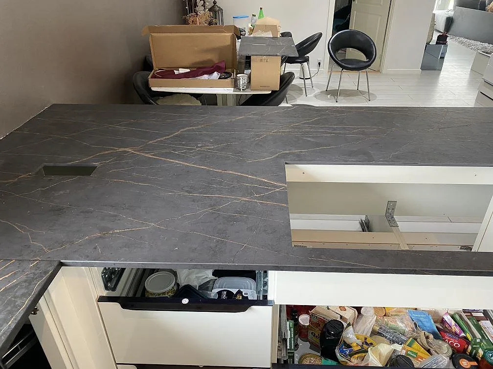 Köksö i Dekton Laurent med matt sintrad keramik och kraftig guld- och kopparådring, fotograferad under montering i ett kök i Vallensbæk.