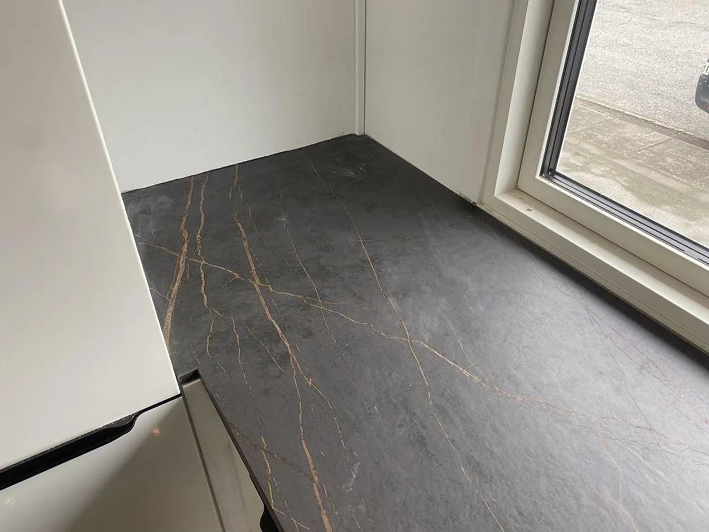 Hörnparti av köksbänkskiva i Dekton Laurent med guldådror mot gråsvart matt keramik i ett kök i Vallensbæk.