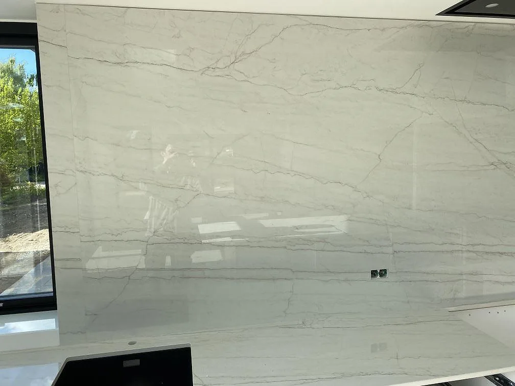 Hög väggbeklädnad i polerad Dekton Limbo keramik med marmorlika grå linjer ovanför köksbänken i Brøndby.