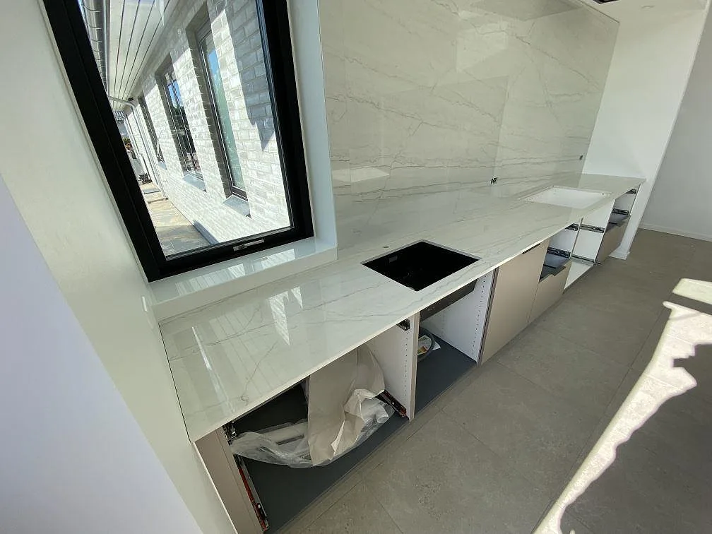 Polerad Dekton Limbo keramik som köksbänkskiva med mörk häll och hög stänkvägg i ett ljust kök i Brøndby.