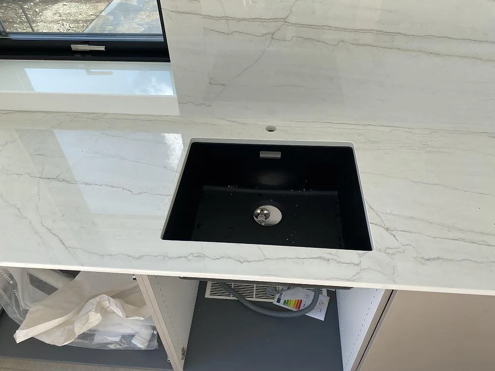 Närbild av svart diskho i polerad Dekton Limbo keramik med ljus ådring och väggbeklädnad i kök i Brøndby.