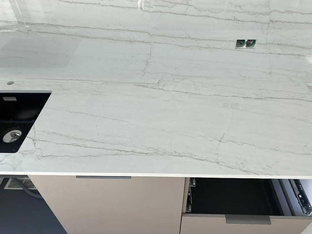 Detalj av ljus Dekton Limbo keramikbänkskiva med grå ådring, svart diskho och polerad yta i Brøndby.