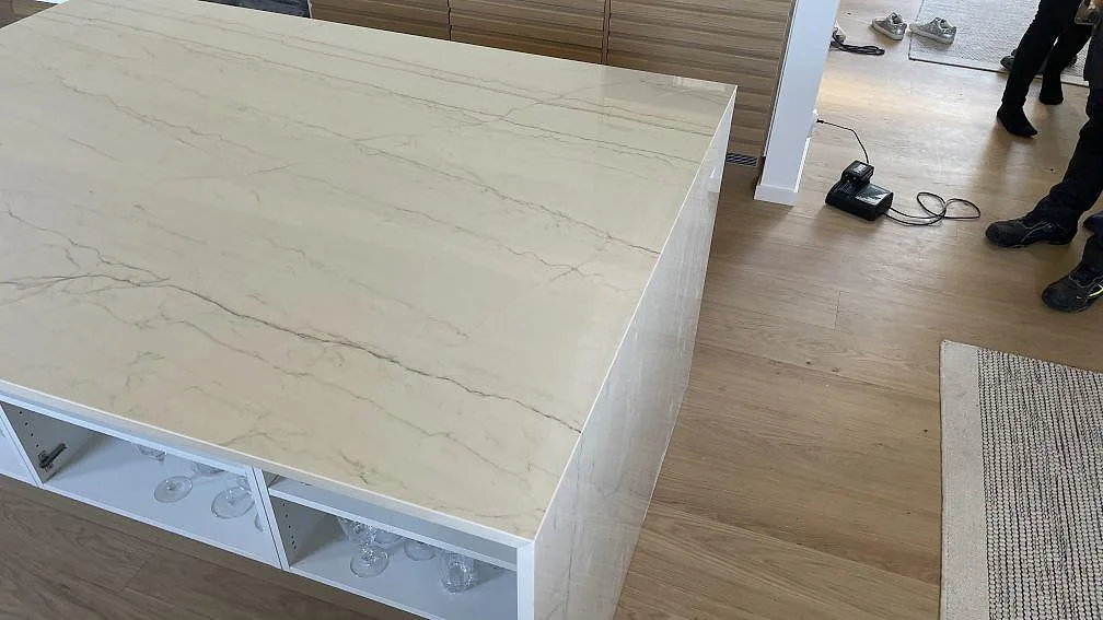 Polerad Dekton Limbo köksö med sammanhängande topp och gavel, ljus ådring och trästommar i Bunkeflostrand.