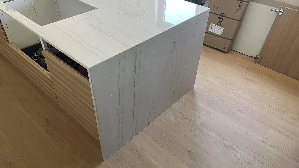 Köksö med neddragen gavel i polerad Dekton Limbo keramik och öppna stommar under montering i Bunkeflostrand.