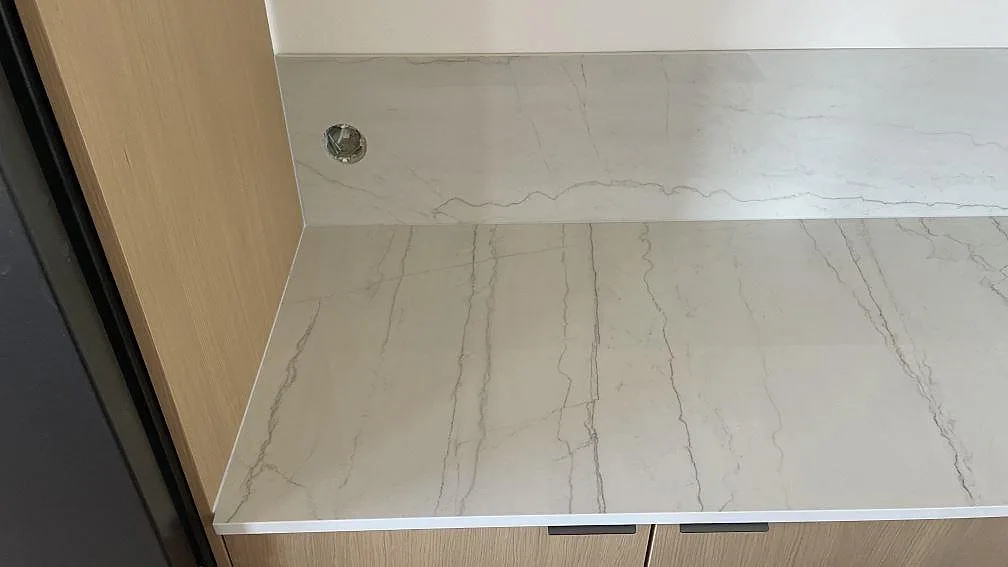 Närbild på polerad Dekton Limbo köksbänkskiva med 8 mm stänkskydd, vägguttag och grå ådring i Bunkeflostrand.