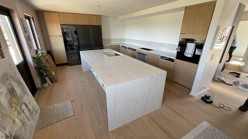Köksbänkskiva i polerad Dekton Limbo keramik med köksö, neddragen gavel och stänkskydd i ett kök i Bunkeflostrand.