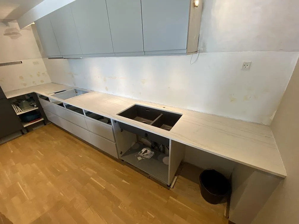 Lång köksbänk i polerad Dekton Limbo längs en ljus vägg, med öppna köksstommar under montering i København s.