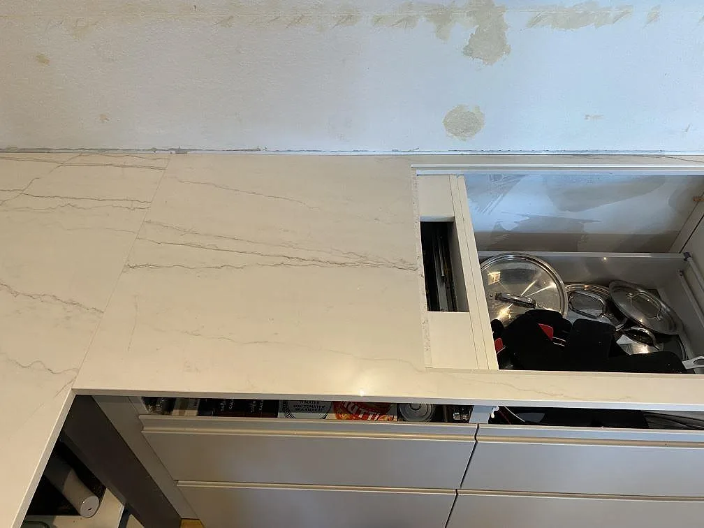 Ovanifrån på den polerade Dekton Limbo skivan vid köksväggen, med ljus keramik och grå ådring i København s.