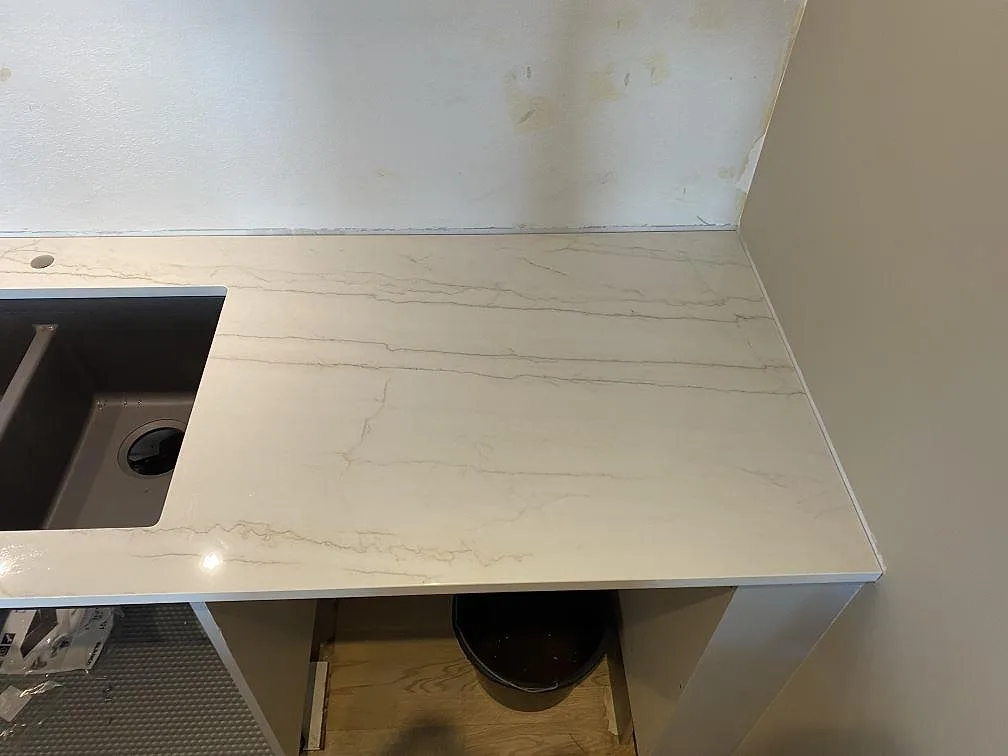 Höger bänksida i polerad Dekton Limbo med ljus grå ådring och öppna underskåp under montering i København s.