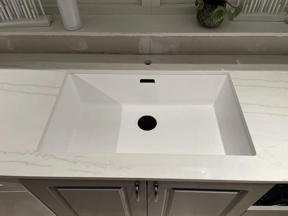 Detaljbild av polerad Dekton Limbo runt hoområdet, vit keramik med grå ådring i ett kök i Nyköping.