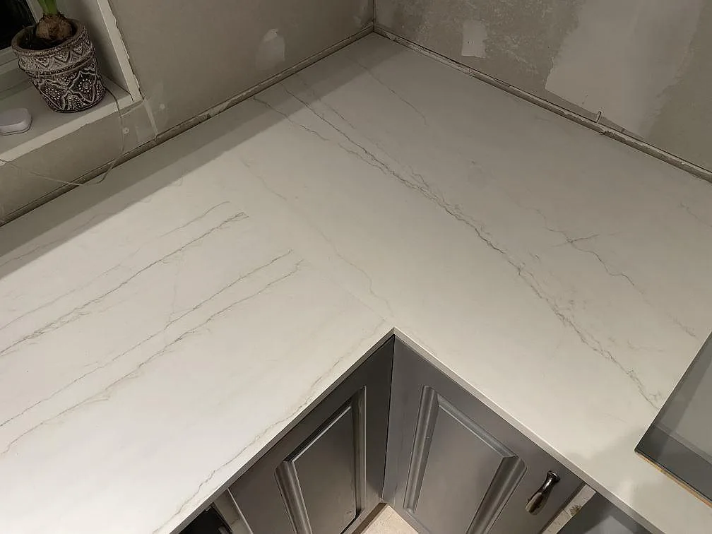 Närbild på hörnpassad köksbänkskiva i polerad Dekton Limbo med ljus marmorlik ådring i Nyköping.