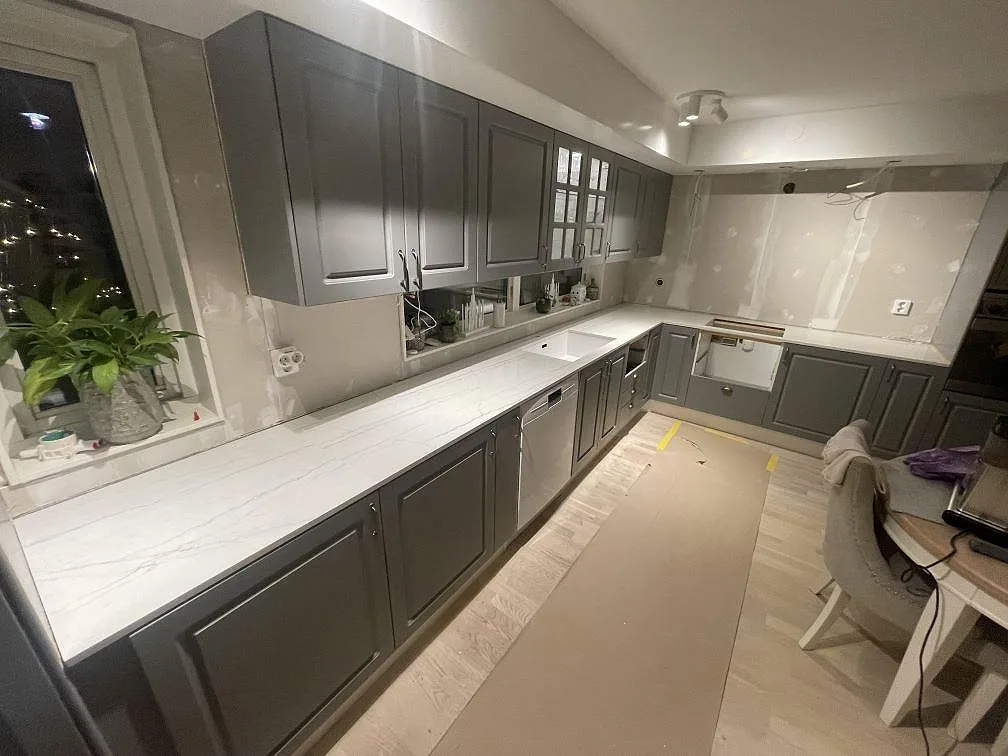 Köksbänkskiva i polerad Dekton Limbo, vit keramik med grå ådring, längs väggarna i ett kök i Nyköping under montering.