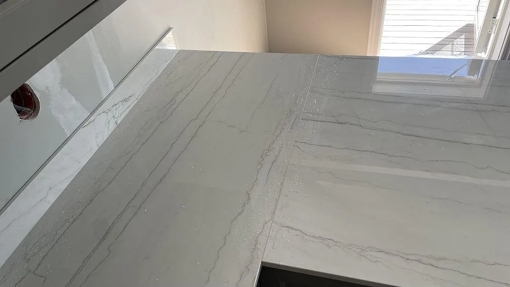 Närbild av polerad Dekton Limbo med grå ådring, vägguppvik och fönsterljus i köket i Örby.