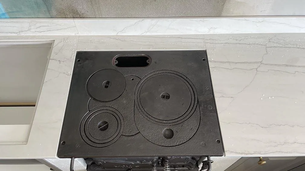 Detalj av polerad Dekton Limbo runt svart spiszon, med låg stänkkant och ljus ådring i Örby.