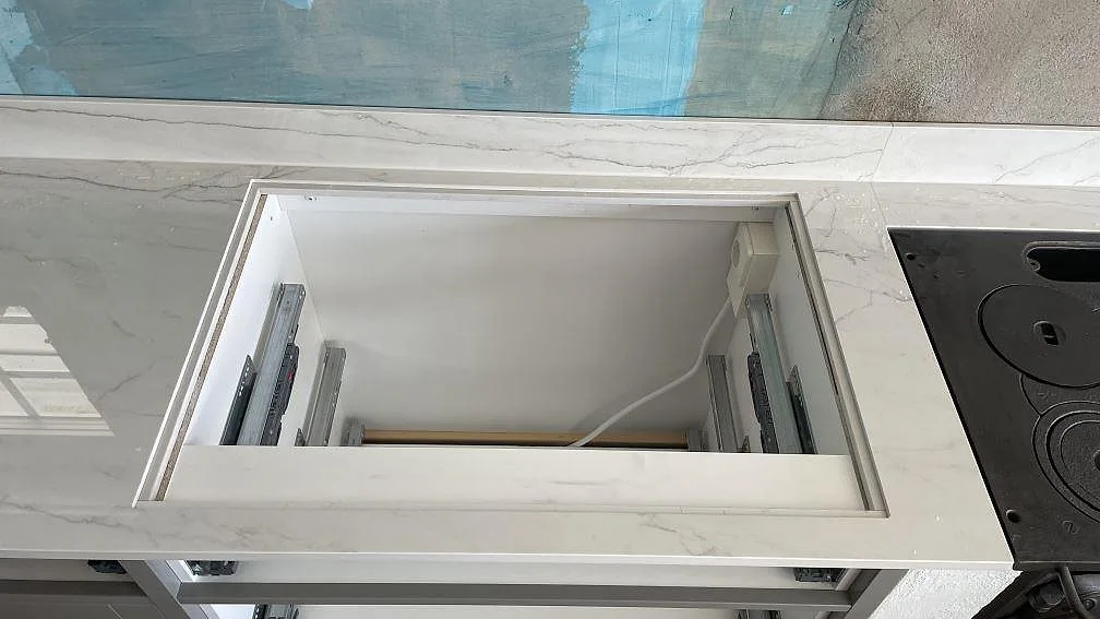 Arbetsyta i polerad Dekton Limbo bredvid svart spiszon, med öppen köksstomme under monteringen i Örby.