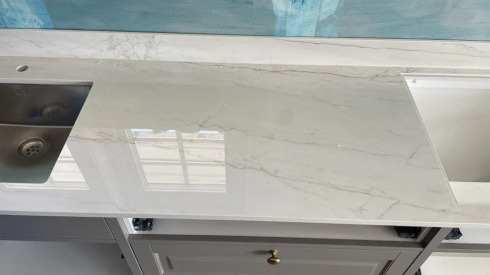 Blank bänkyta i Dekton Limbo mellan rostfri diskho och intilliggande urtag i köket i Örby.
