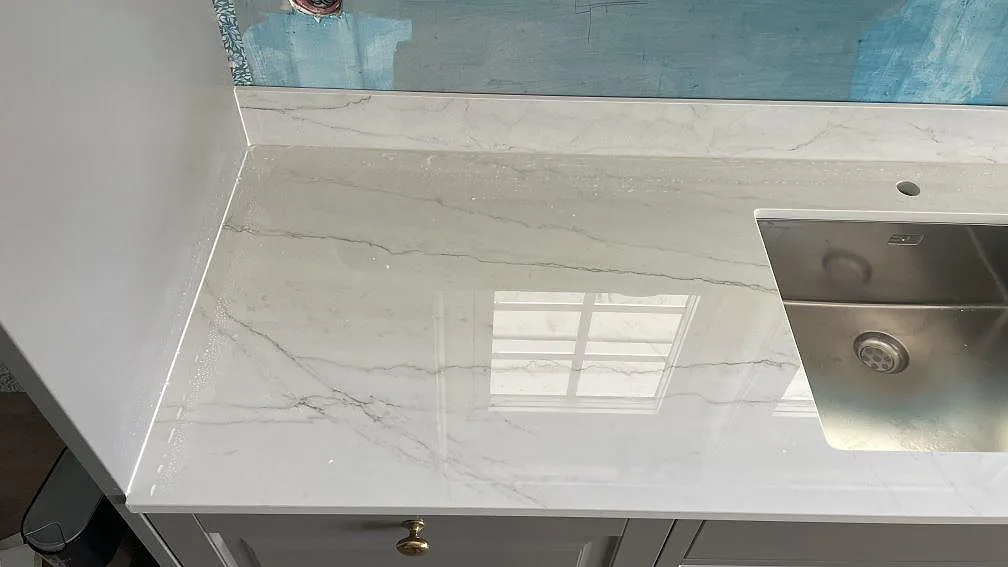 Polerad Dekton Limbo vid rostfri diskho, med vägguppvik och fönsterreflektion i köket i Örby.