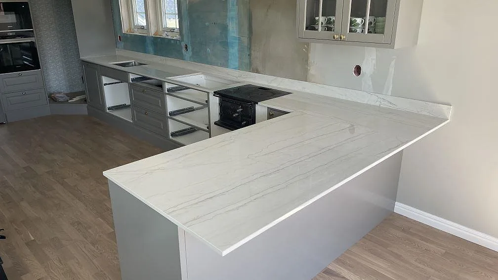 Köksbänkskiva i polerad Dekton Limbo med halvö, låg stänkkant och grå köksstommar i Örby.