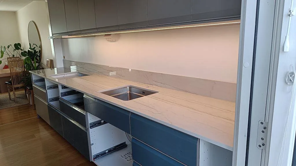 Köksbänkskiva i polerad Dekton Limbo keramik med stänkskydd, diskho och hällöppning i ett kök i Rydebäck.