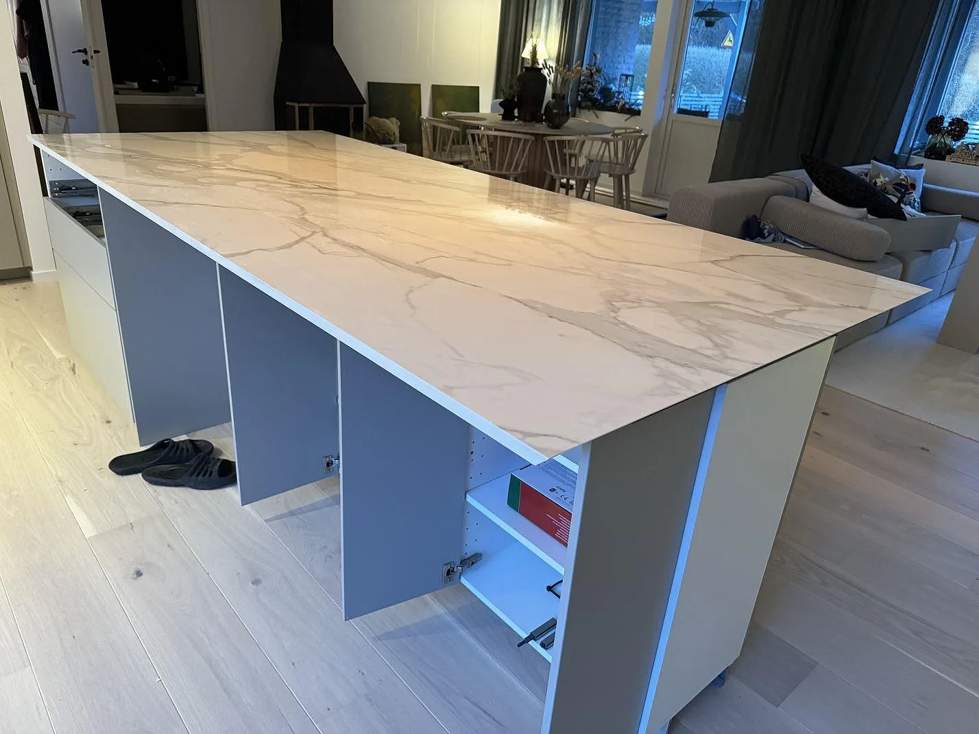 Stor köksö med polerad vit Dekton Lucid keramik och grå ådring i ett kök under montering i Löddeköpinge.