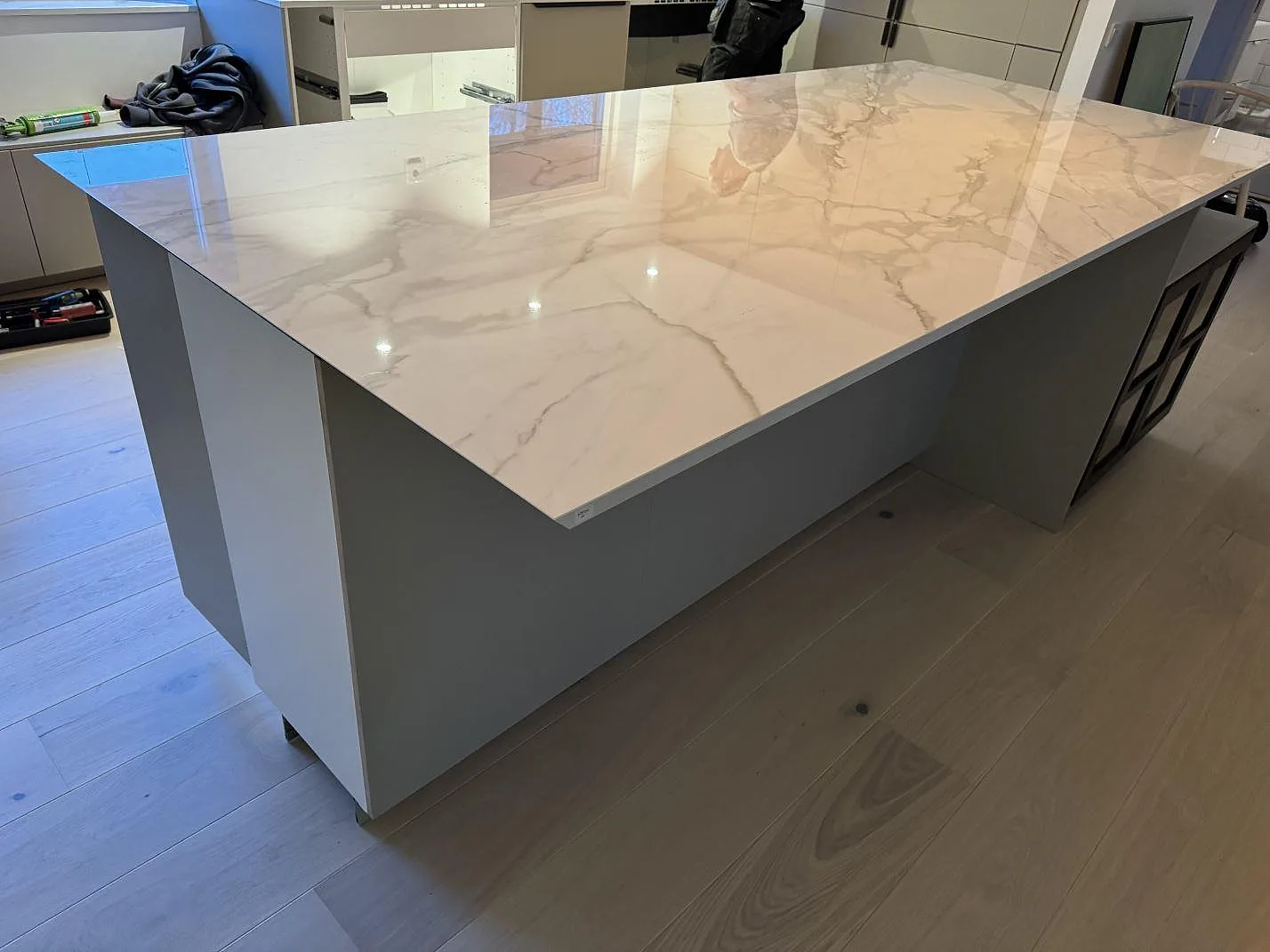 Närbild på polerad Dekton Lucid som köksö med blank vit keramisk yta och öppna skåpstommar i Löddeköpinge.