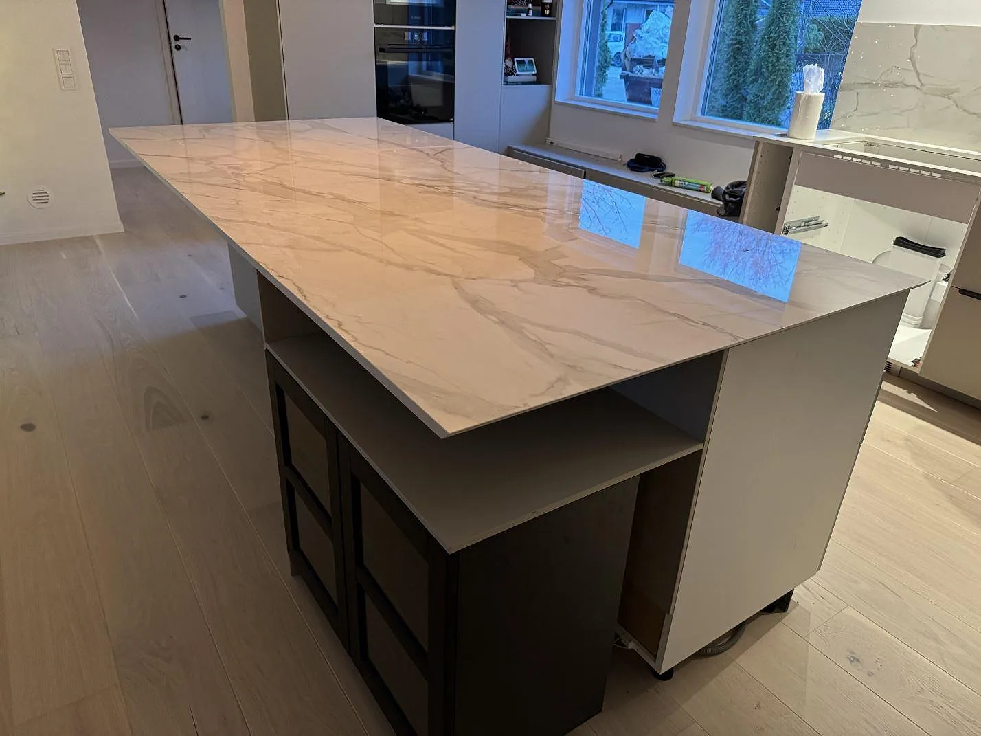 Lång köksö i polerad vit Dekton Lucid keramik framför bänkar och fönster i ett kök i Löddeköpinge.