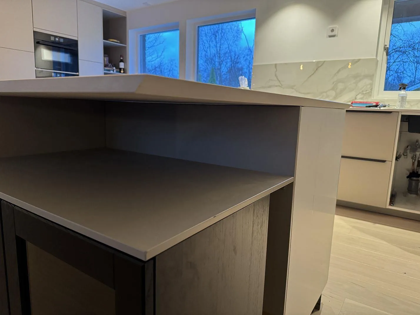 Låg vinkel på köksö och väggbänk i polerad Dekton Lucid keramik under montering i Löddeköpinge.