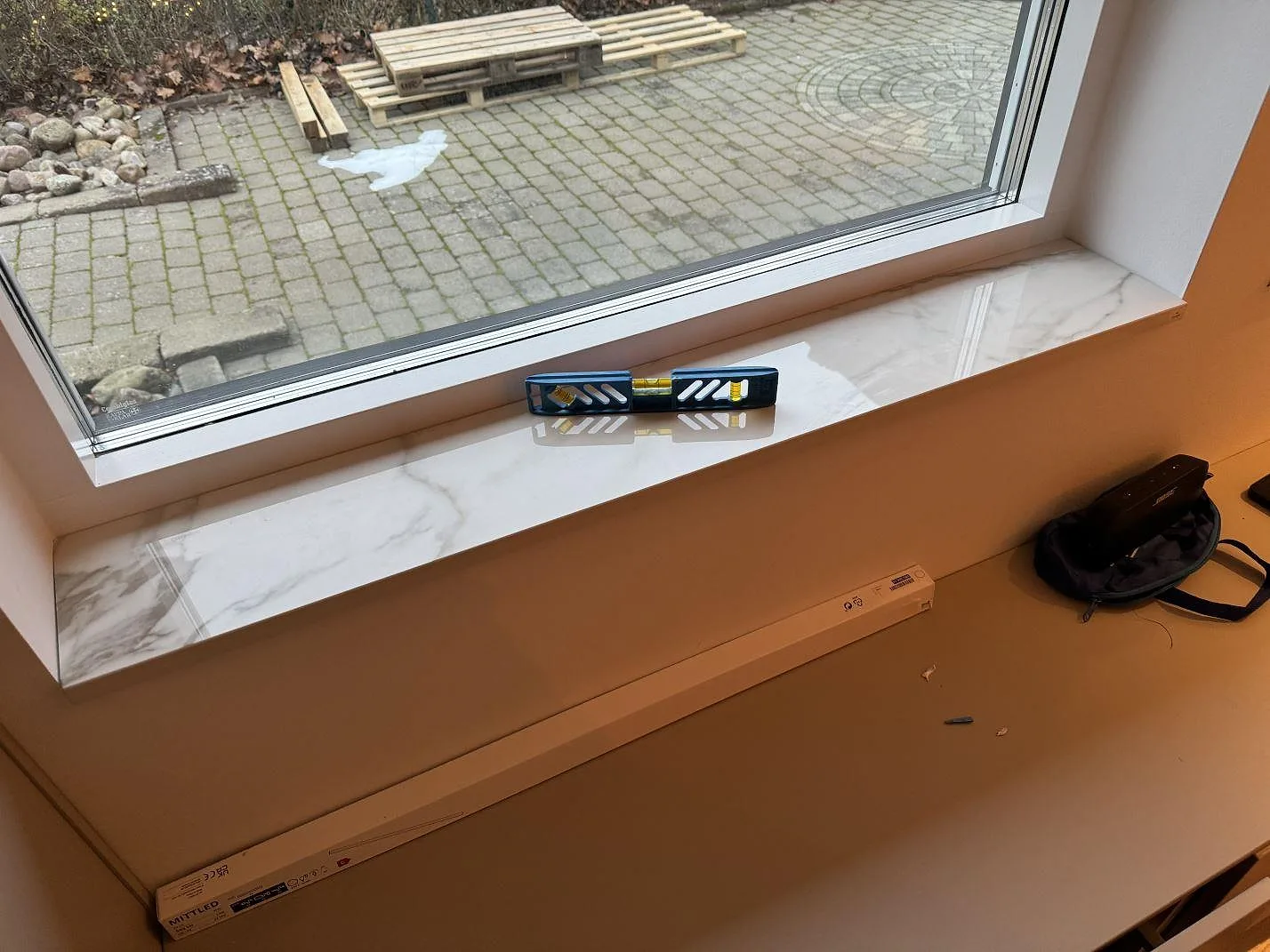Fönsterbänk i polerad Dekton Lucid keramik med vit botten, grå ådring och monteringsverktyg i Löddeköpinge.