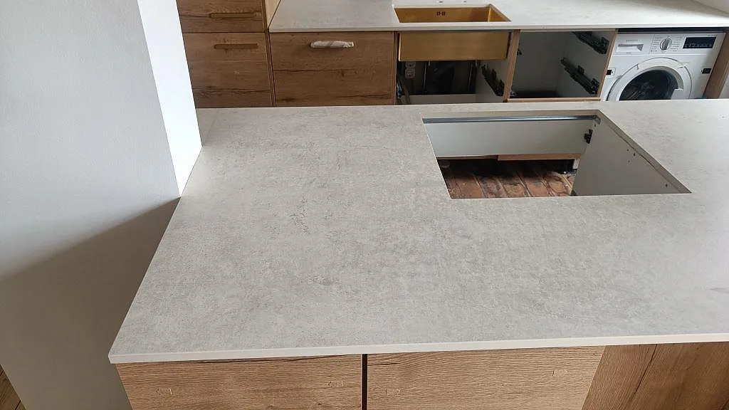 Närbild på matt Dekton Lunar som köksbänkskiva på halvö med förberedd öppning och träskåp i København Ø.