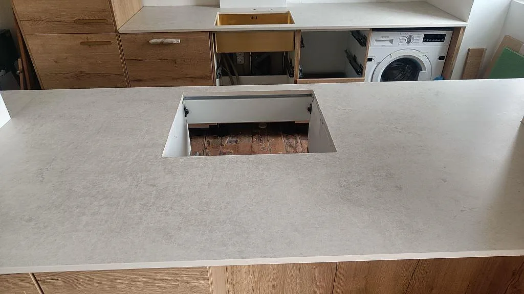 Matt köksbänkskiva i Dekton Lunar med stor öppning i halvön, underlimmad diskho bakom och integrerad tvättmaskin i København Ø.