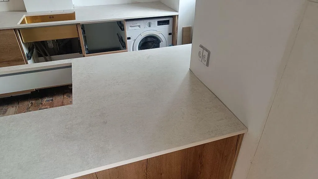 Dekton Lunar i matt keramik på kökshalvö med ljus väggyta, träinredning och synlig bänkrad i København Ø.