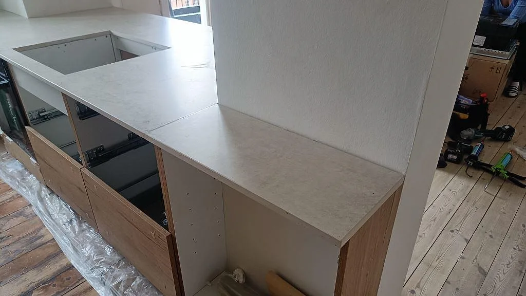 Köksbänkskiva i matt Dekton Lunar runt väggparti med öppna trästommar och monteringsverktyg i København Ø.