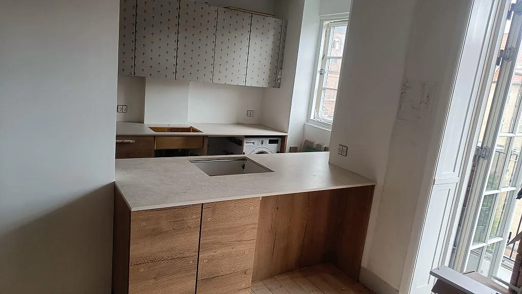 Köksbänkskiva i matt Dekton Lunar, 20 mm keramik, med halvö, underlimmad diskho och träinredning i København Ø.