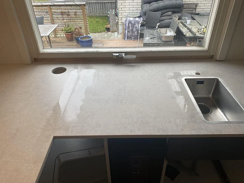 Köksbänkskiva i grå Dekton Lunar med urtag för diskho och induktionshäll under montering i ett kök i Sävedalen.